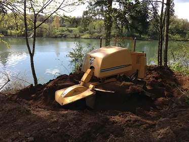 Stump grinder at work beside a pond